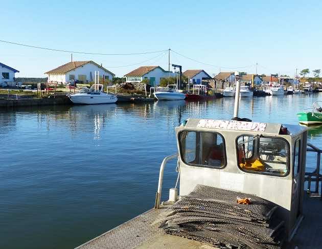 Vue des cabanes du port ostréicole d'Arès à marée haute, avec une plate, bateau utilisé par les ostréiculteurs.